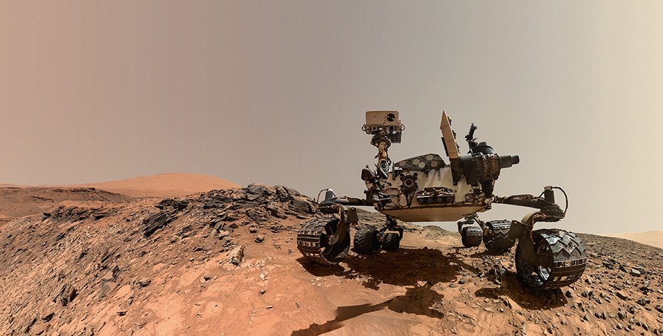 Curiosity made this self-portrait on August 5, 2015, by maneuvering the Mars Hand Lens Imager (MAHLI) camera on the end of a seven-foot-long robotic arm. Multiple overlapping frames were acquired, then digitally stitched together by image analysts at JPL. The arm moved into a new position for each frame but the camera always pointed toward a specific “vanishing point” to minimize parallax distortions. Copyright: NASA